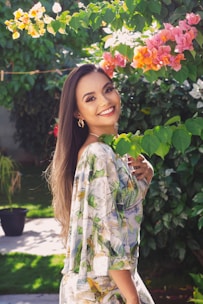 A cheerful woman wearing a flowing floral dress, standing in a sunlit garden