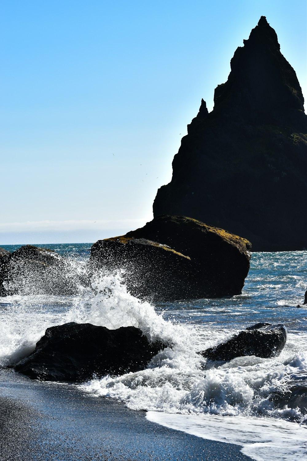 a large rock sticking out of the ocean next to a beach