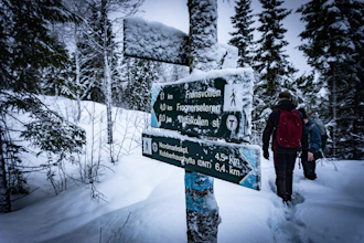 A family wearing warm gear navigating a snowy trail marked with safety signs.