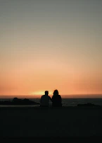 A sunset silhouette of a couple enjoying a quiet moment on a beach, embodying calm and connection.