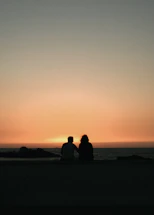 A sunset silhouette of a couple enjoying a quiet moment on a beach, embodying calm and connection.