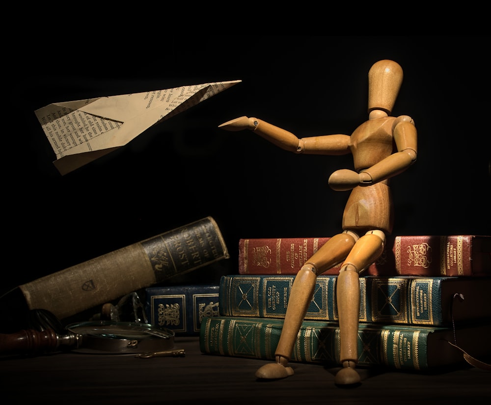 a wooden doll sitting on top of a pile of books