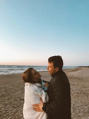 A couple watching a sunset on a quiet beach, wrapped in a cozy blanket