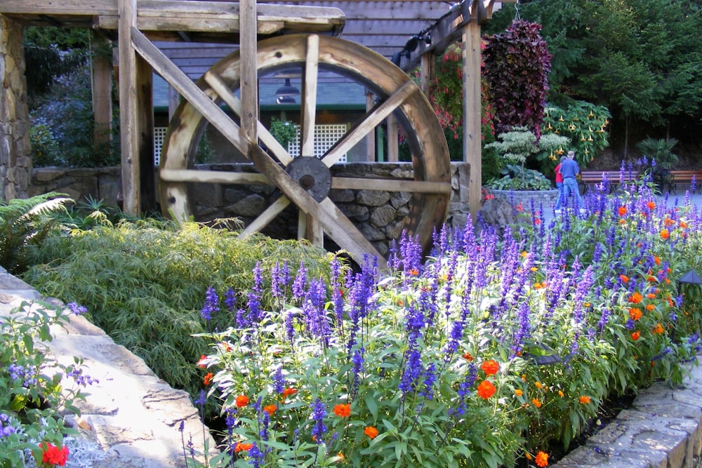 a garden filled with lots of flowers and a water wheel