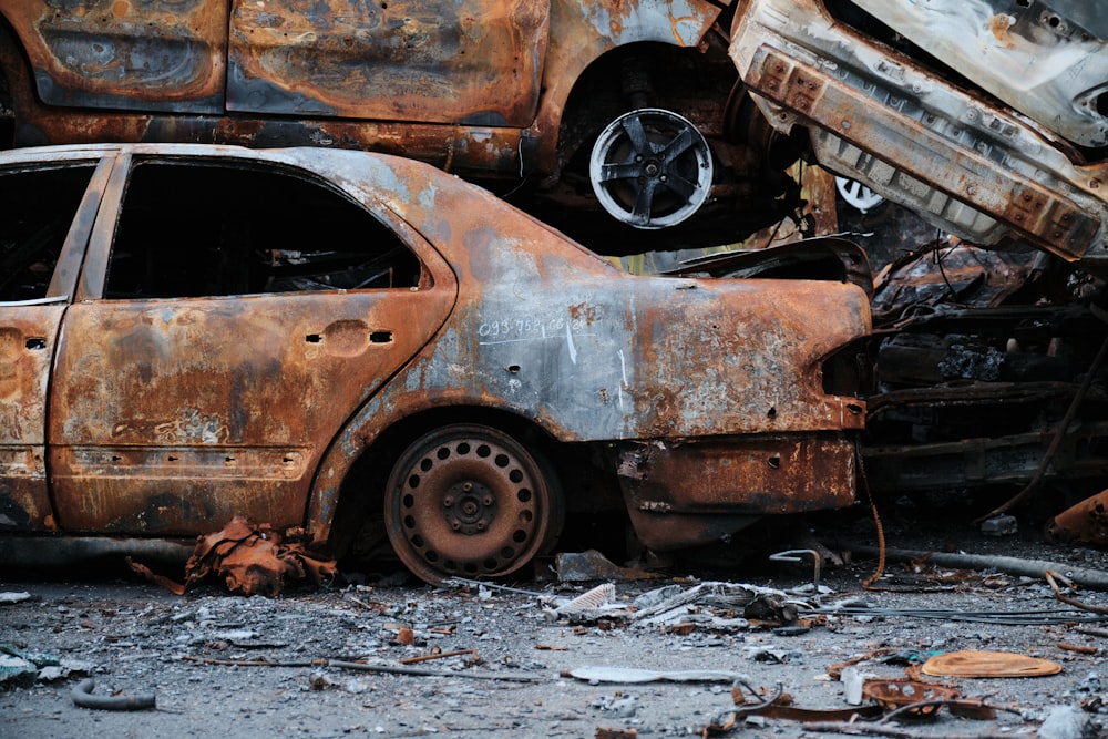 a rusted out car sitting in the middle of a pile of junk
