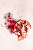 Fresh pomegranate seeds bursting out beside a deep red juice bottle.