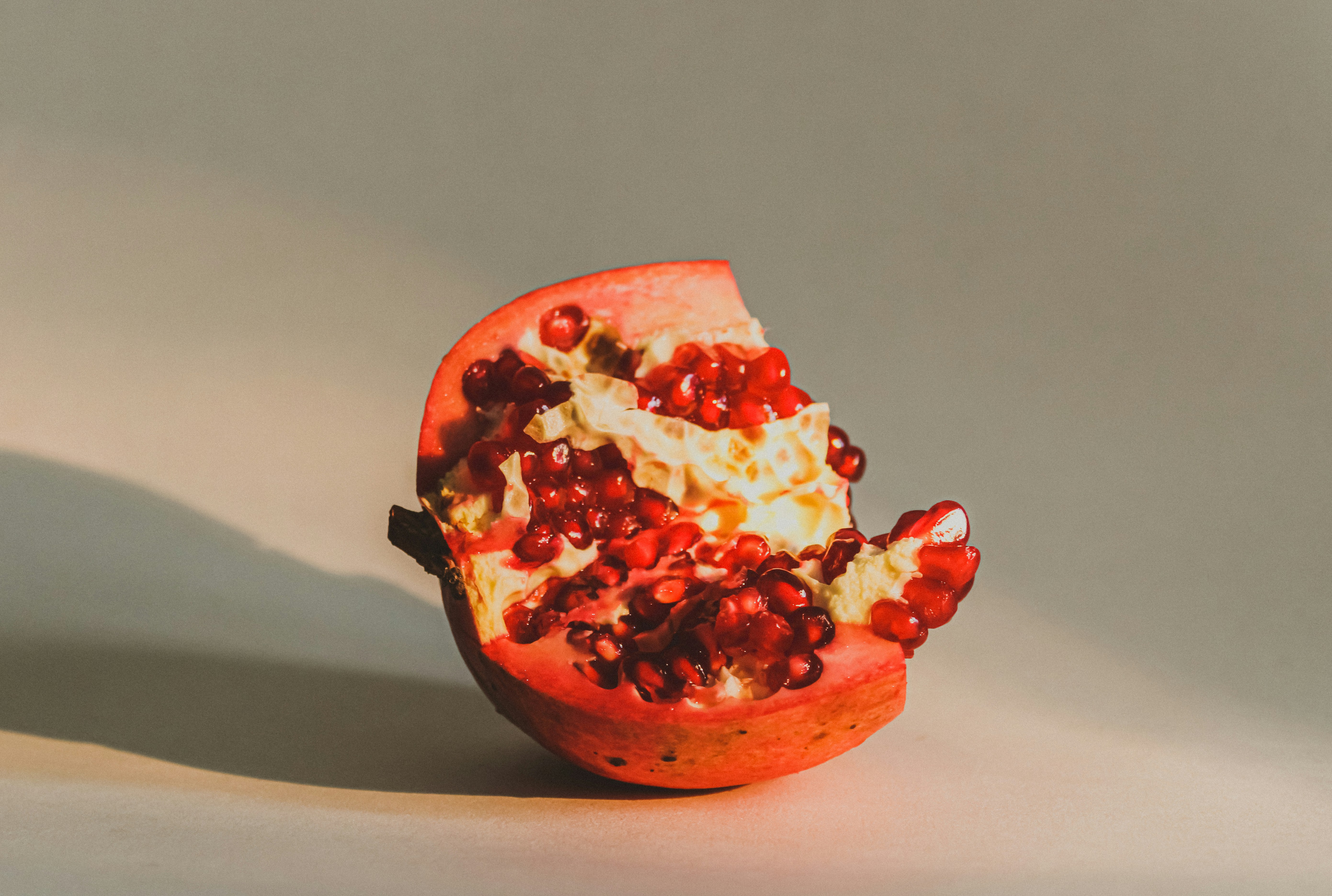 Cut pomegranate revealing ruby red seeds on a white marble surface, bright clean light