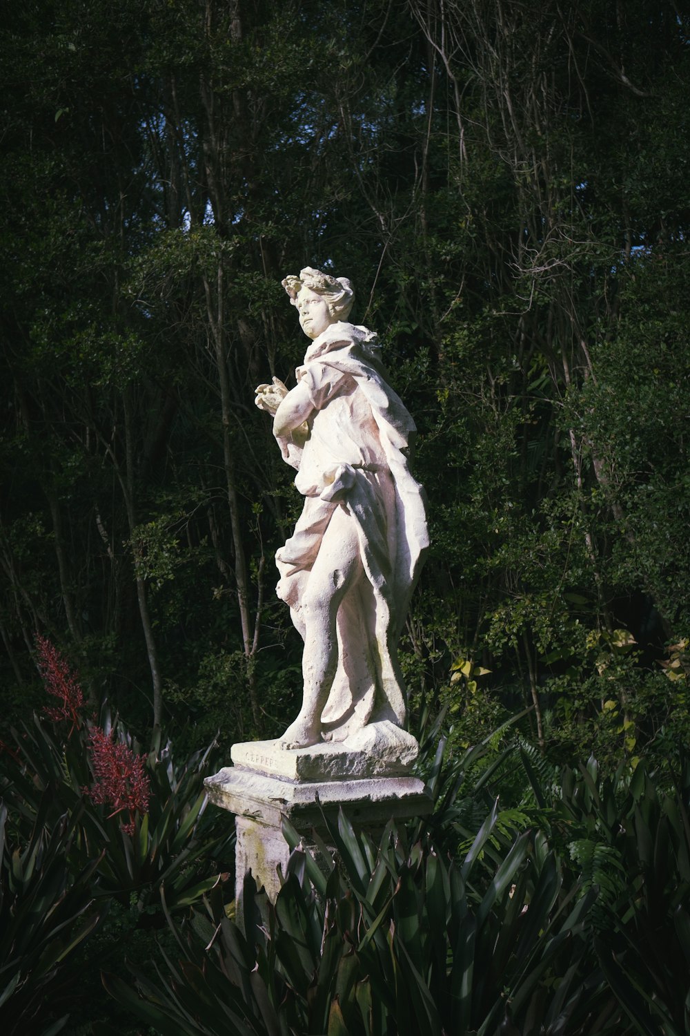 a statue of a woman holding a bird in a forest