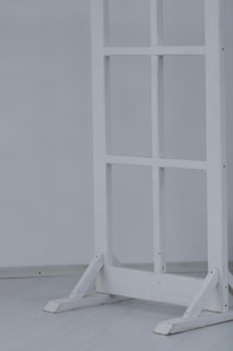 A wooden frame resembling a window or partition stand sits on a light-colored floor. The structure has several square sections and is painted white.