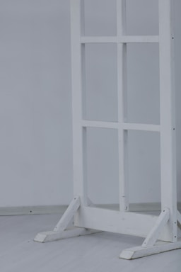 A wooden frame resembling a window or partition stand sits on a light-colored floor. The structure has several square sections and is painted white.