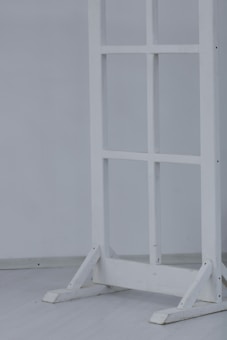 A wooden frame resembling a window or partition stand sits on a light-colored floor. The structure has several square sections and is painted white.