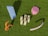Several abstract and colorful objects are placed on a green grassy surface. The objects include a large light blue curved shape, a pink gear-like object, an orange spiral, a cluster of vertical cream-colored sticks arranged in a grid, and a curved light pink tube.