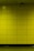 A yellow tiled wall with a small rectangular access panel and a security camera mounted near the ceiling. The tiles are arranged in a grid, and there is a reflective, polished floor at the bottom.