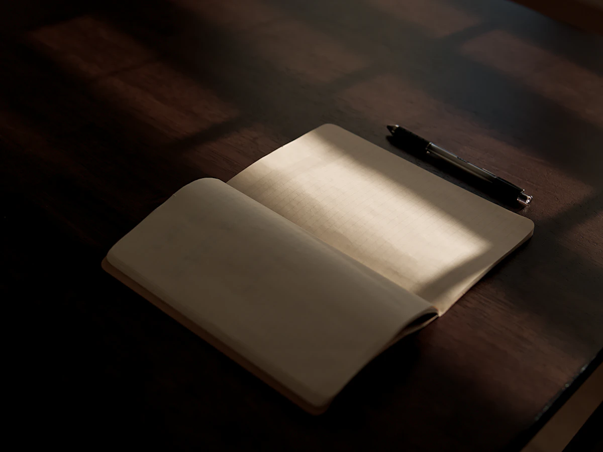 Ein geöffnetes leeres Notizbuch und ein Stift auf einem Holztisch im Licht
