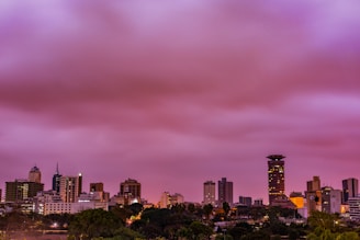 A cinematic night city skyline featuring a modern university campus glowing under deep purple and charcoal skies.