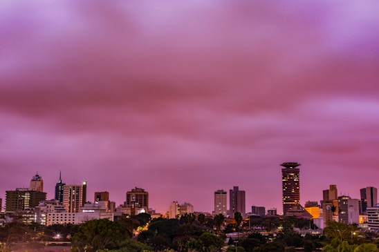 A cinematic night city skyline featuring a modern university campus glowing under deep purple and charcoal skies.