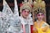 Two people dressed in traditional Chinese opera costumes stand side by side. The ornate costumes feature intricate patterns, vibrant colors, and elaborate headpieces adorned with jewels and feathers. Both individuals have bold, theatrical makeup emphasizing their eyes and eyebrows.