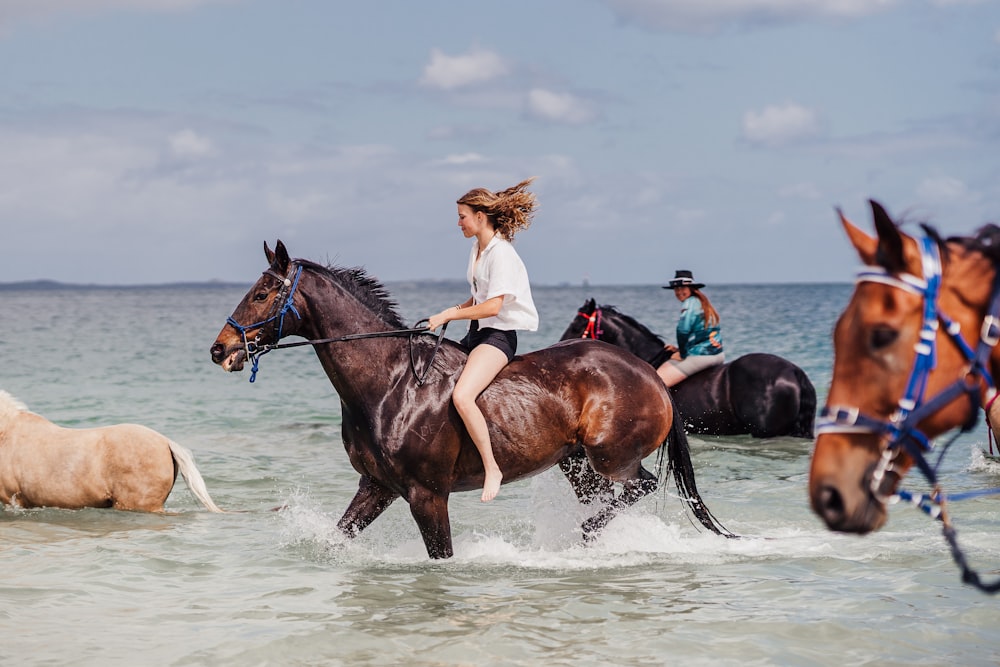 a group of people riding horses through a body of water