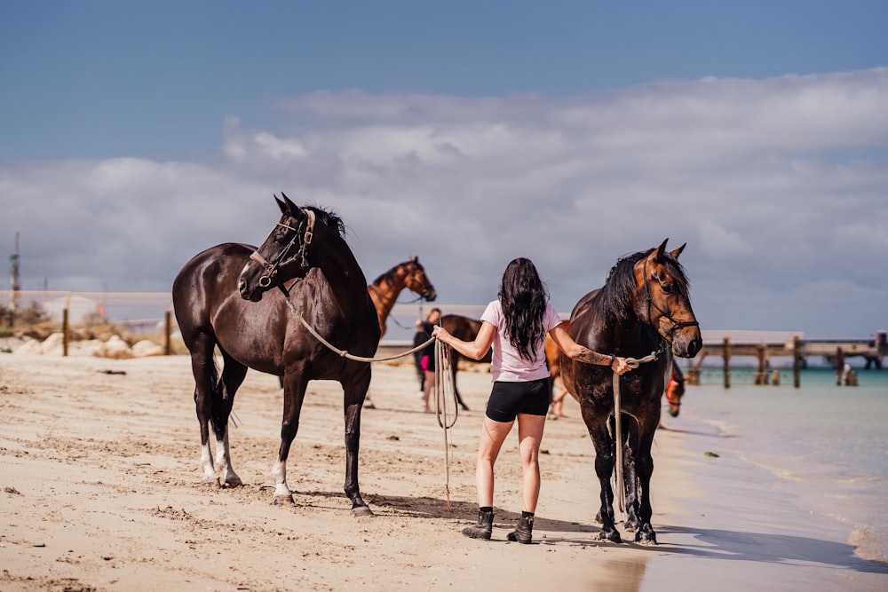 a woman leading two horses on a beach