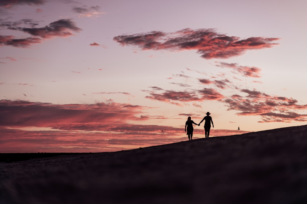 two people holding hands while standing on a hill