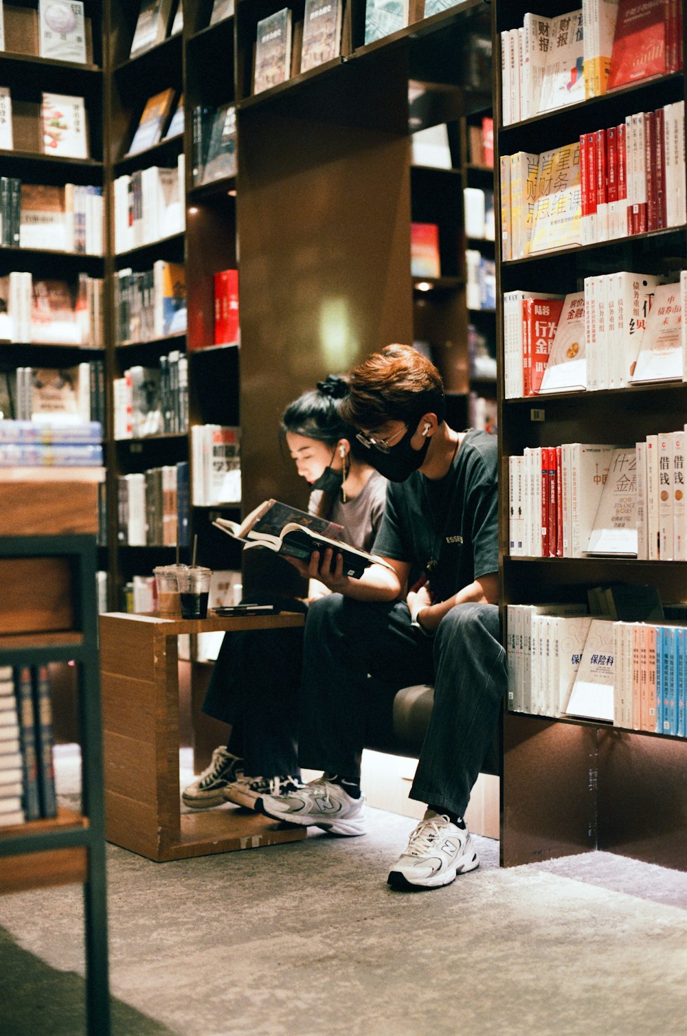 two people sitting on a bench in front of a bookshelf