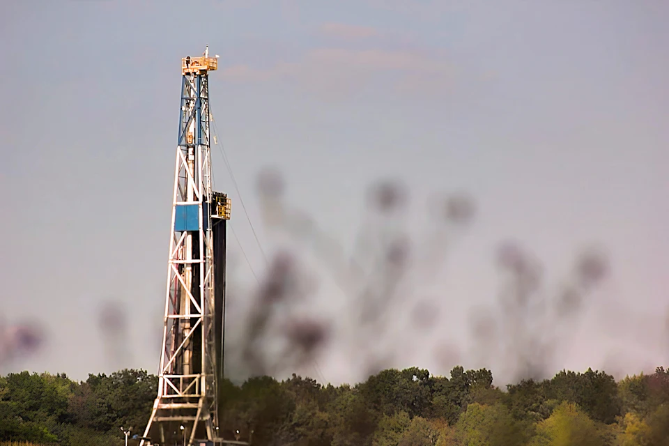 Drilling rig mast seen across a field at dusk