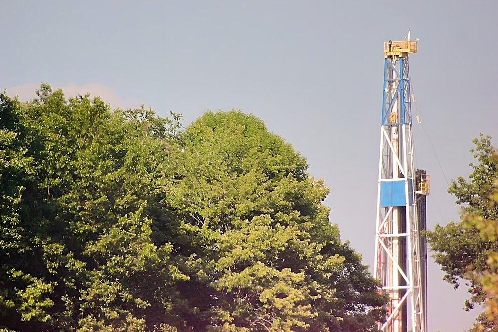 a blue and white drilling rig next to trees