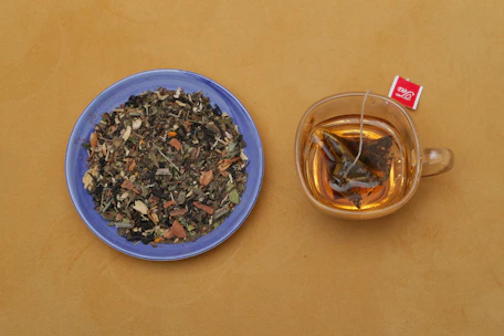 A person preparing a vibrant cup of herbal tea with fresh ingredients on a wooden table.
