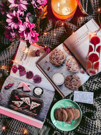 A bright kitchen nook with fresh flowers, a homemade candle, and a stack of recipe books inviting homemaking inspiration.