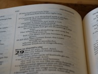 An open book displaying text from a religious scripture, specifically from the Old Testament. The verses discuss teachings and instructions from God, describing various practices including threshing. The text is in a clean, legible font with chapter and verse numbers clearly marked.
