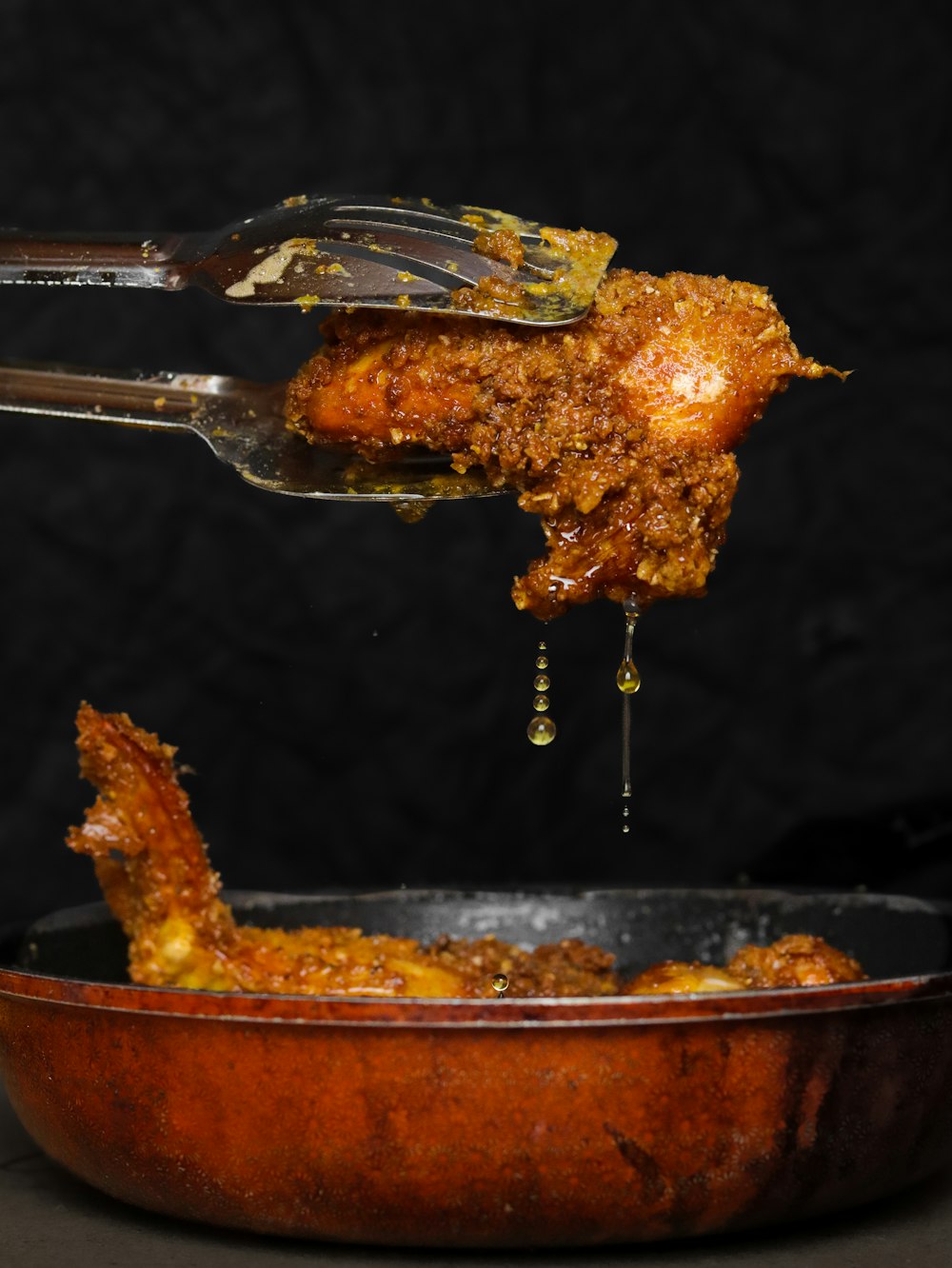 a piece of chicken being lifted from a skillet