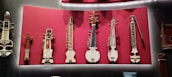 A collection of stringed musical instruments displayed on a vibrant red background. The instruments vary in shape and size, with intricate detailing and diverse structural designs, suggesting traditional craftsmanship.