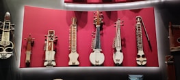 A collection of stringed musical instruments displayed on a vibrant red background. The instruments vary in shape and size, with intricate detailing and diverse structural designs, suggesting traditional craftsmanship.