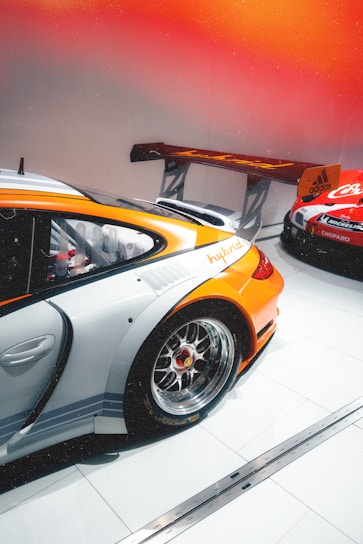 A sleek, dark-themed photo of the Gualotuna Motorsports team preparing their race cars under orange accent lighting.