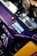 A close-up view of a car engine bay, showcasing a purple metallic component with a glossy finish and metallic flecks. There is a blue and white informational label on the surface, as well as visible bolts and brackets for securing the part. Other engine components and metallic surfaces are partially visible in the background.