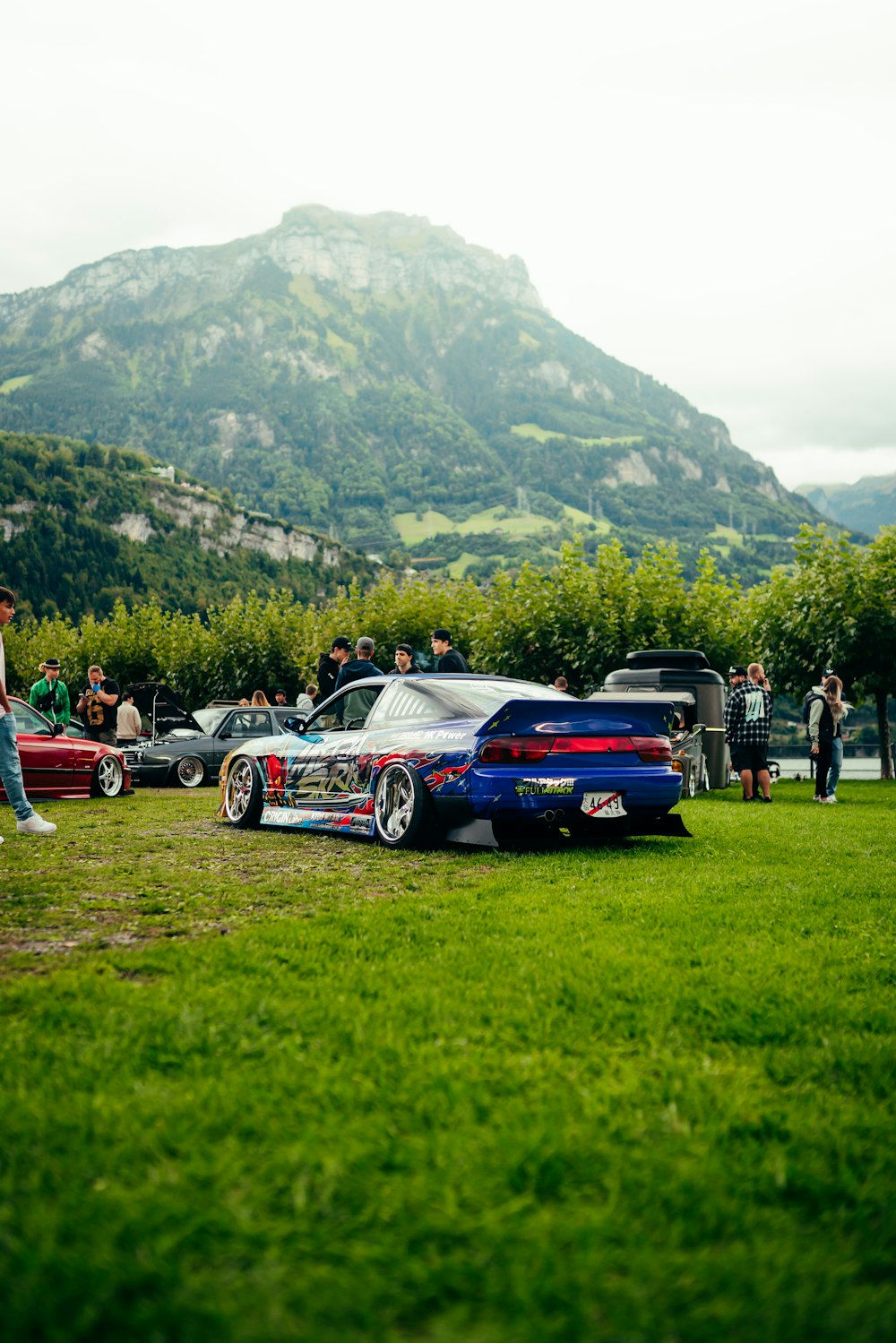 um grupo de carros estacionados em um campo ao lado de uma montanha