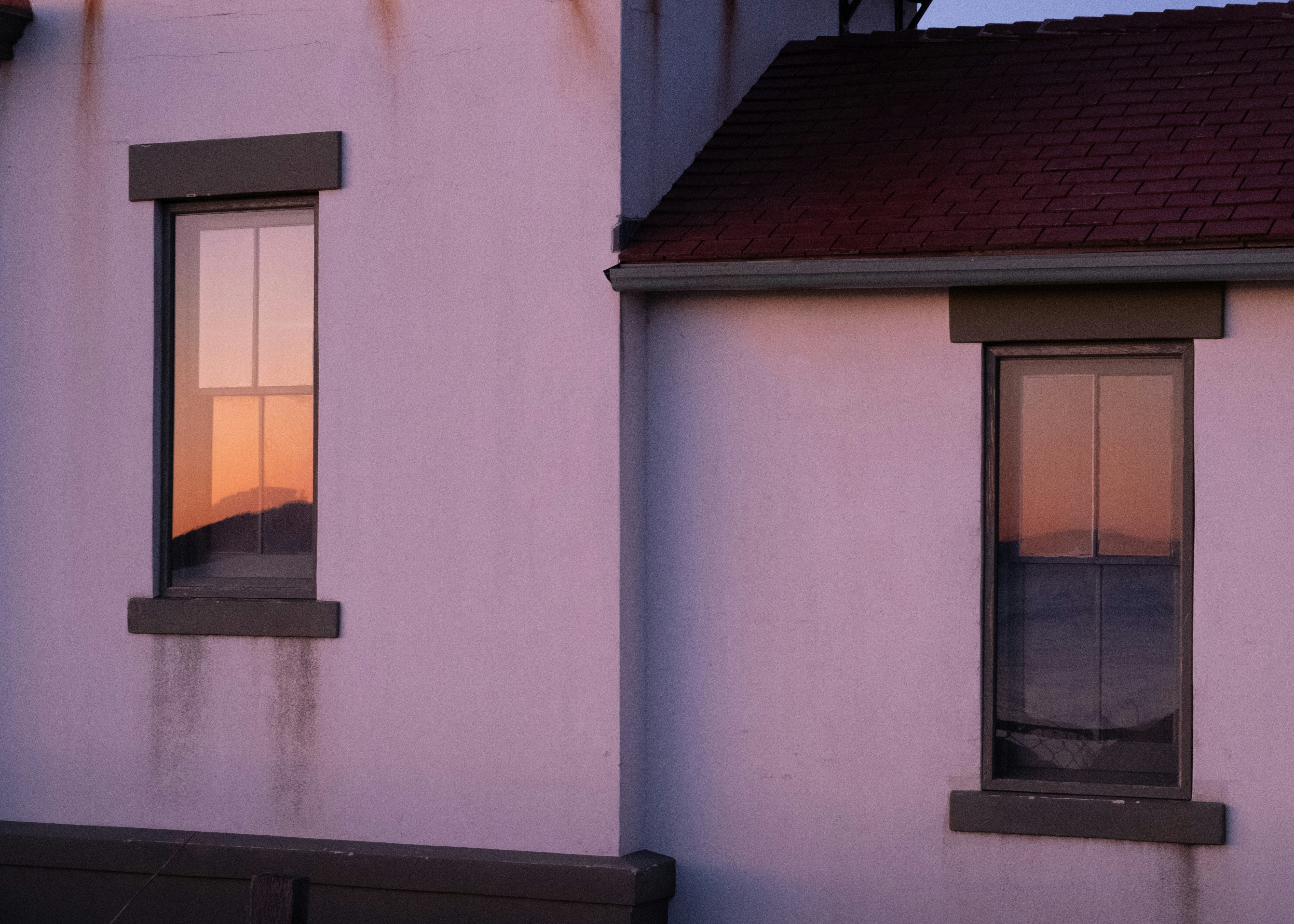 a white building with two windows and a red roof