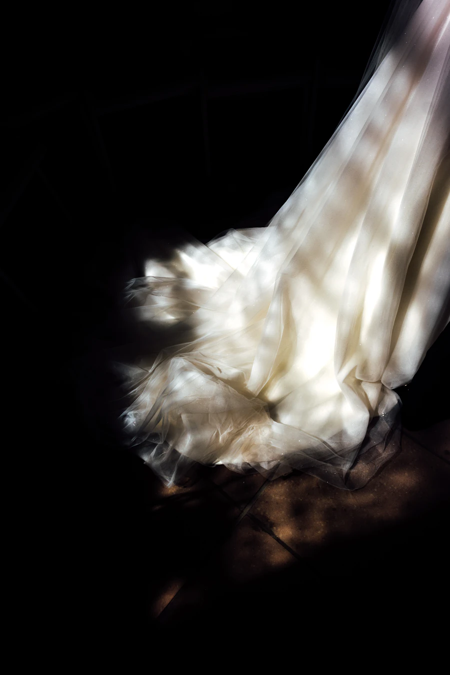 An editorial bridal portrait — luminous white dress emerging from shadow