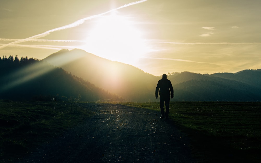 a man walking down a dirt road towards the sun