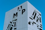 A modern building with a minimalist facade featuring large cut-out letters and abstract shapes against a clear blue sky. The building has a sleek, geometric design.