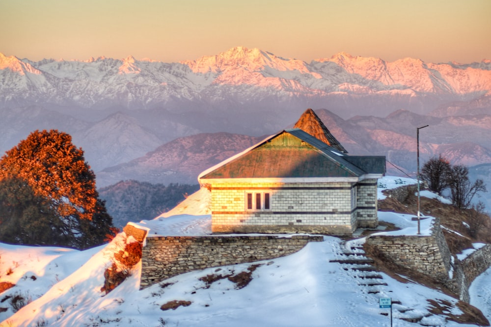 a house on a snowy mountain with mountains in the background