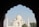 A view of the Taj Mahal framed by a dark archway silhouette, highlighting its symmetrical architecture and iconic white marble dome. The sky is clear with a few trees visible at the base of the structure.