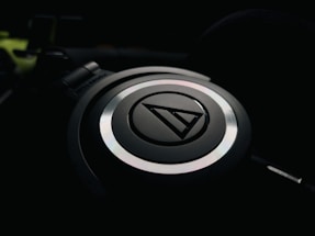 A close-up of a headphone with a circular design, featuring a logo at the center. The image captures only one side of the headphones, highlighting its sleek design in low lighting.