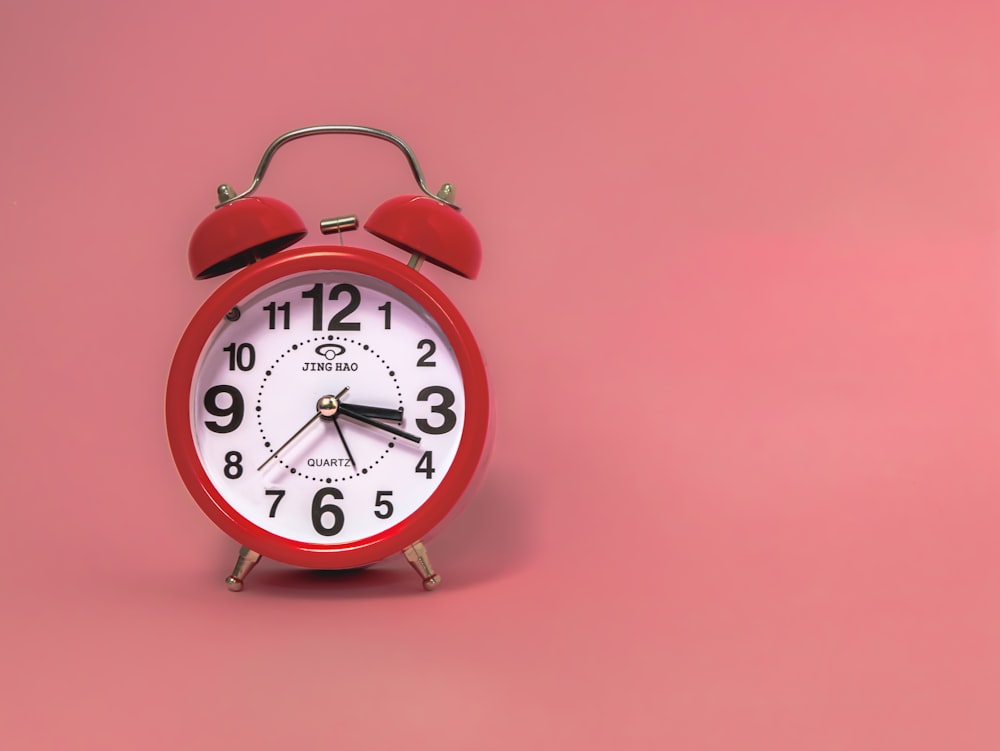 a red alarm clock on a pink background
