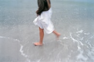 A relaxed figure walking barefoot along the shoreline, waves gently touching their feet.