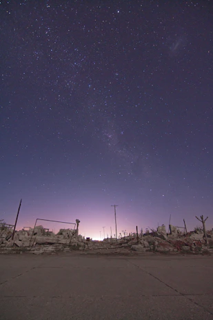 A starry night sky over an ancient ruin illuminated by soft purple and blue hues.