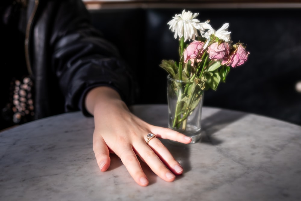 a woman's hand on a table with a vase of flowers