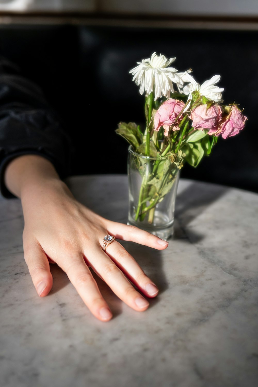 a woman's hand on a table with a vase of flowers