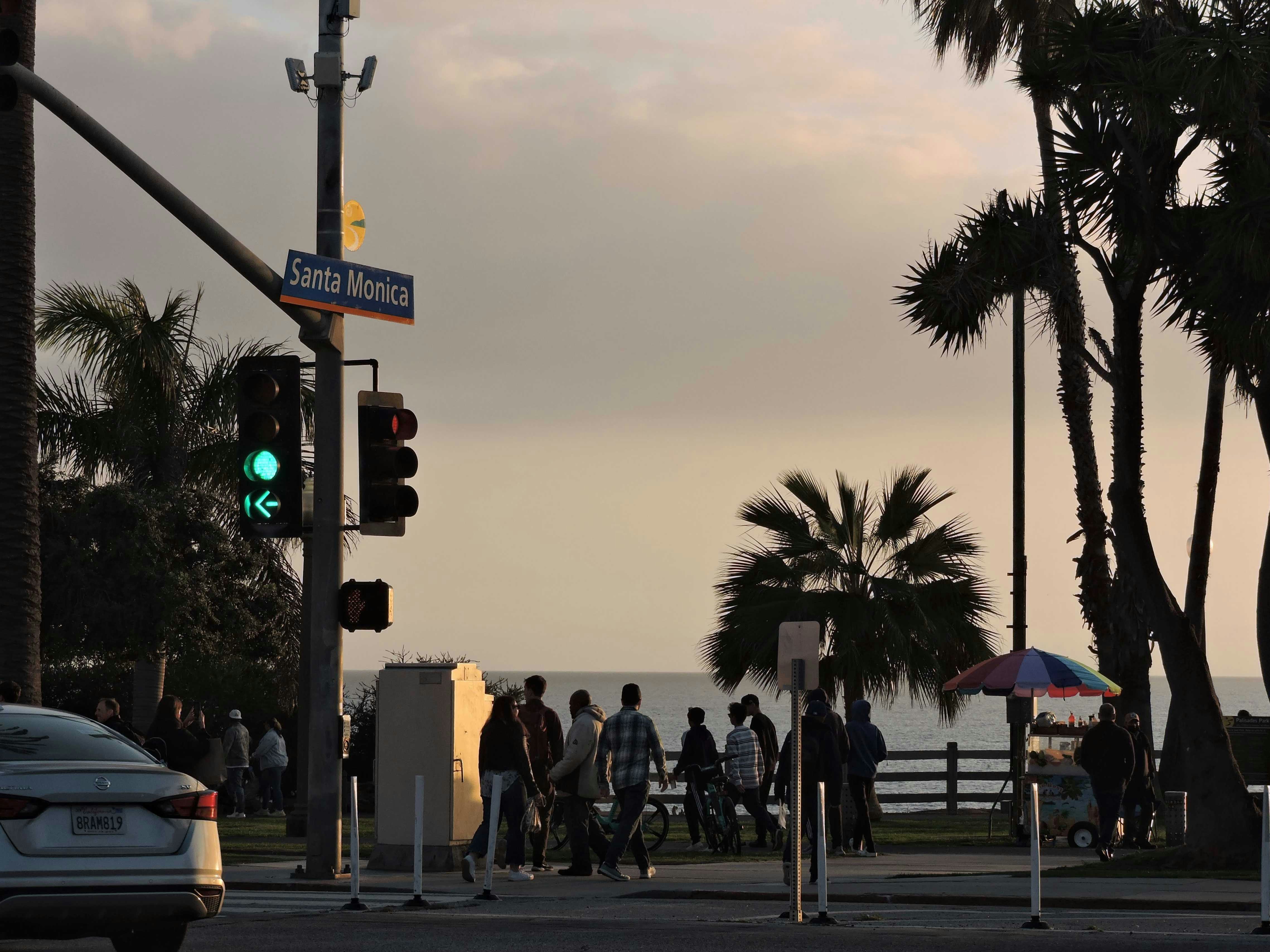 a group of people walking across a street next to palm trees