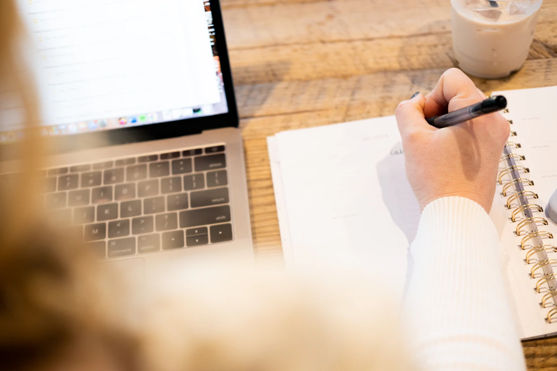 Personne travaillant sur un ordinateur et rédigeant des notes à côté du clavier
